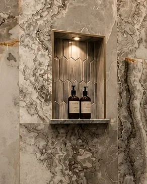 Second lit shower niche with a hexagon-patterned back wall and a stone shelf set flush into the surrounding wall tile.